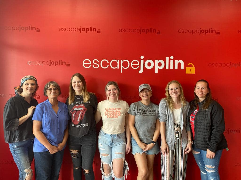 A group of women standing in front of an escape joplin sign.